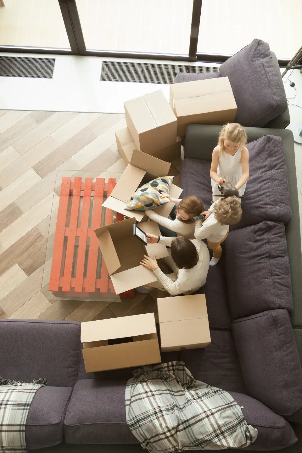 Une famille est occupée à emballer des cartons dans un salon, avec des enfants et des adultes aidant à l'organisation.